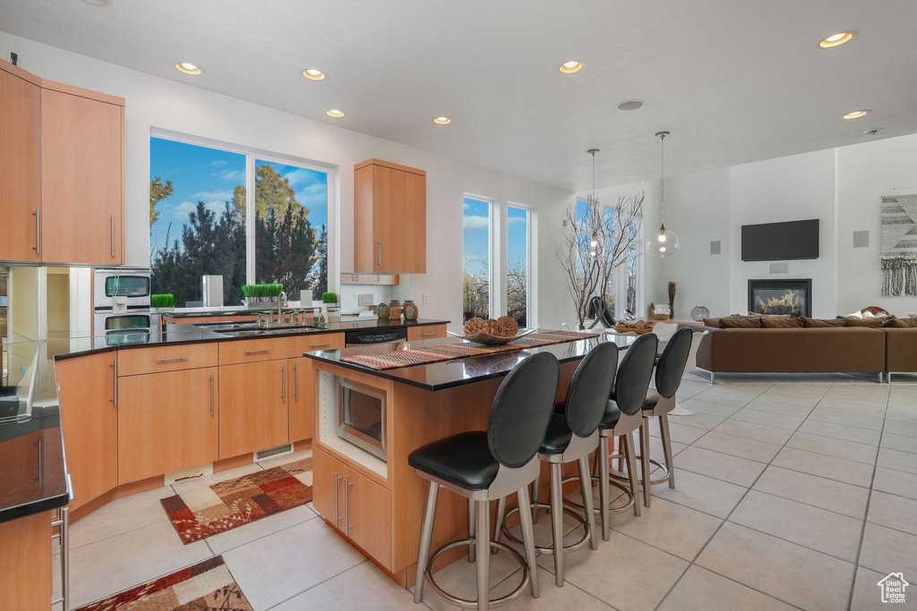 Kitchen featuring a sink, light tile patterned floors, dark countertops, recessed lighting, and a center island