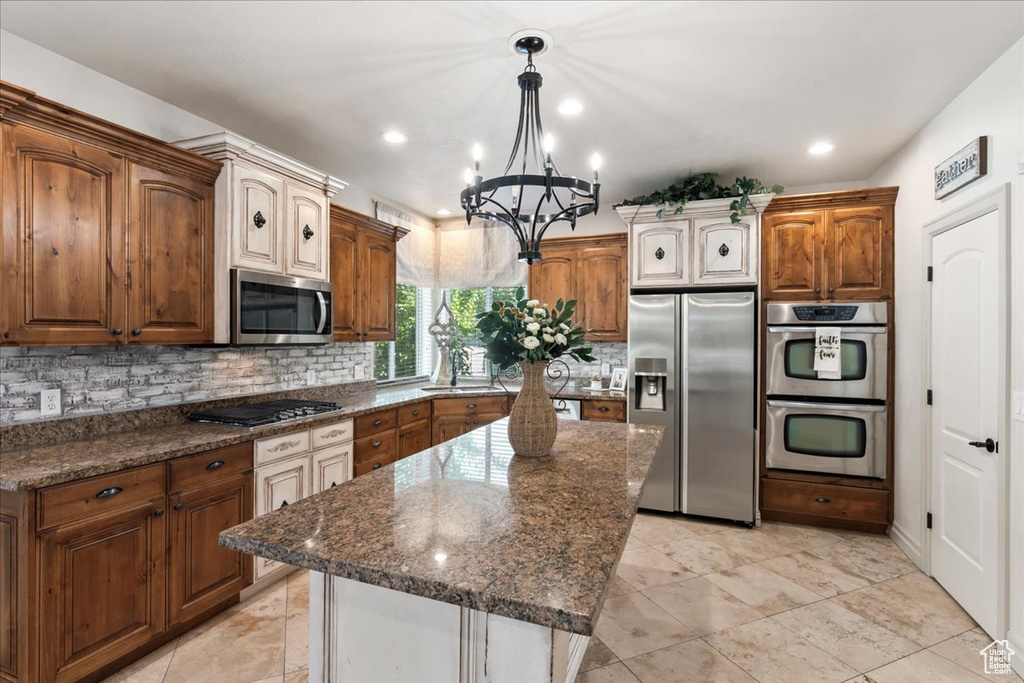 Kitchen with stainless steel appliances, backsplash, a chandelier, a sink, and dark stone countertops