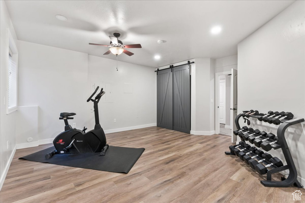 Exercise area with a ceiling fan, light wood finished floors, a barn door, baseboards, and recessed lighting