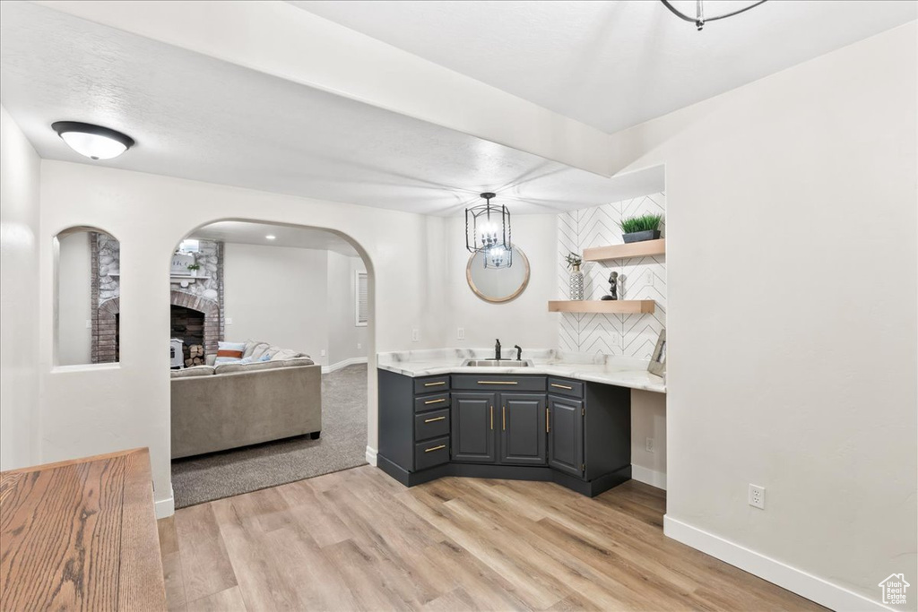 Bar area with a sink, a large fireplace, light wood-type flooring, and arched walkways
