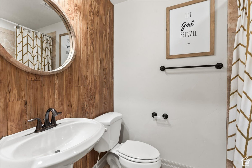 Bathroom featuring a sink, baseboards, toilet, and wood walls