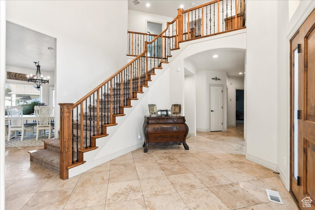 Tiled entrance foyer featuring a towering ceiling, stairway, arched walkways, a chandelier, and baseboards