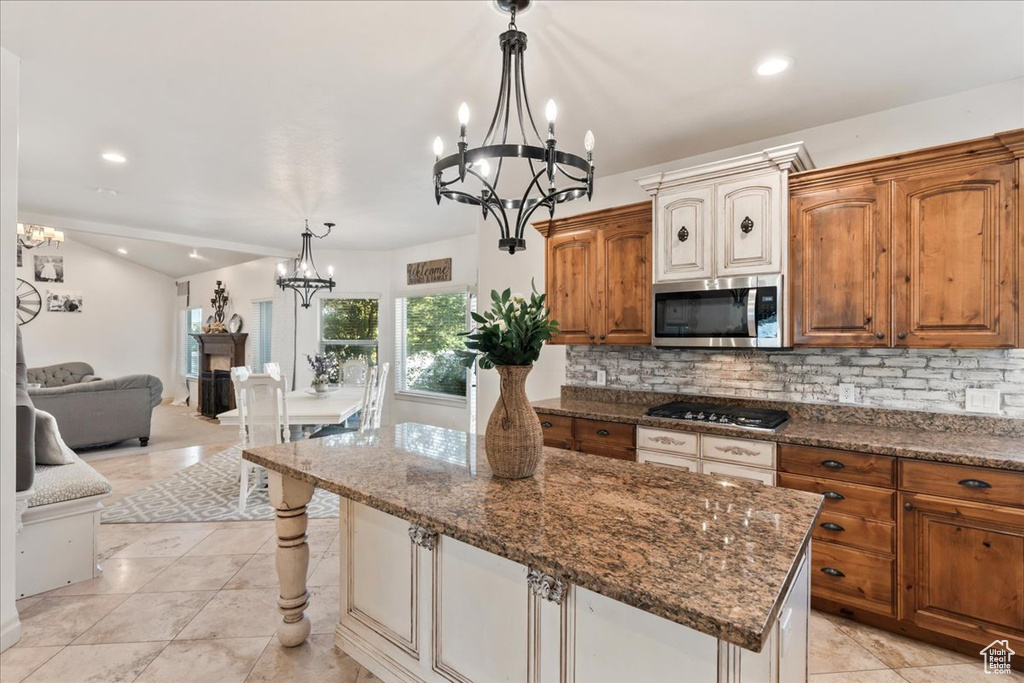 Kitchen with stainless steel microwave, a chandelier, gas cooktop, tasteful backsplash, and dark stone countertops