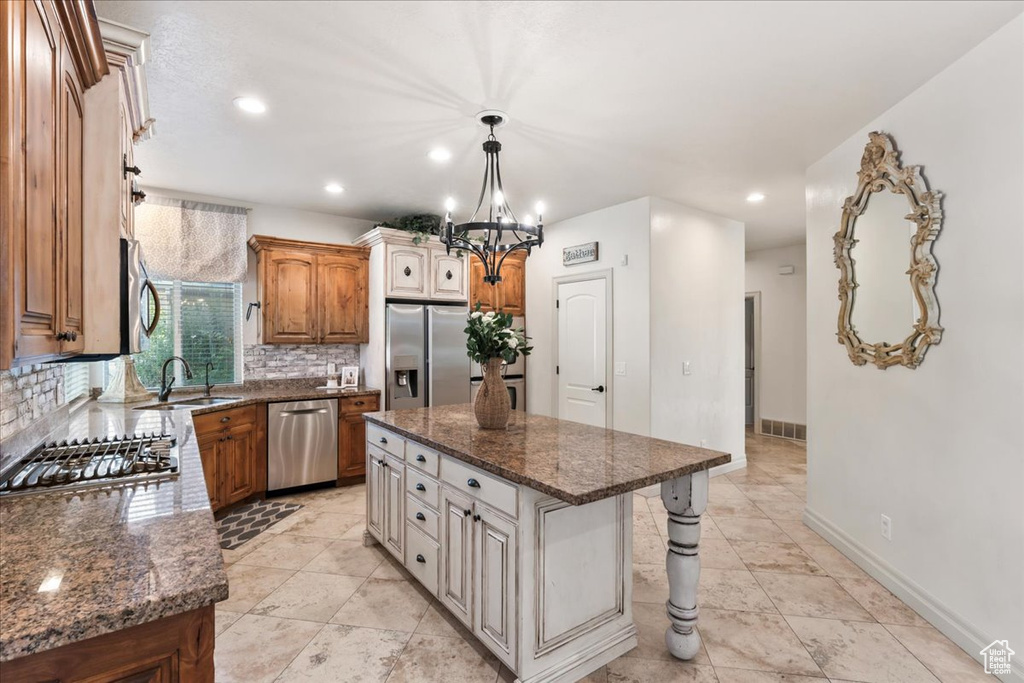 Kitchen with appliances with stainless steel finishes, a sink, decorative backsplash, a chandelier, and dark stone counters