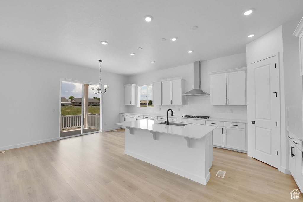 Kitchen featuring wall chimney range hood, a sink, gas stovetop, light countertops, and recessed lighting