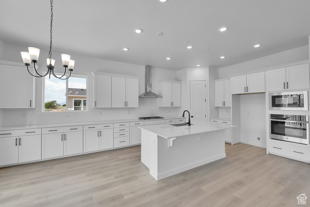 Kitchen featuring wall chimney range hood, oven, a sink, built in microwave, and gas cooktop