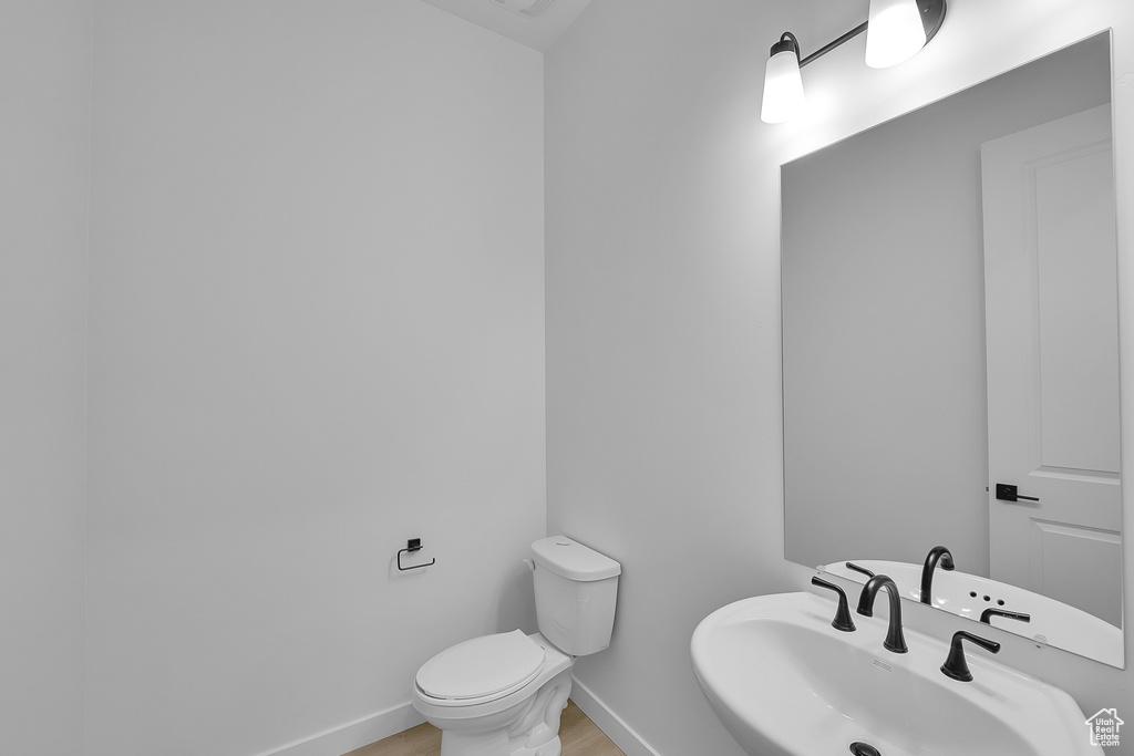 Half bathroom featuring toilet, a sink, baseboards, and wood finished floors