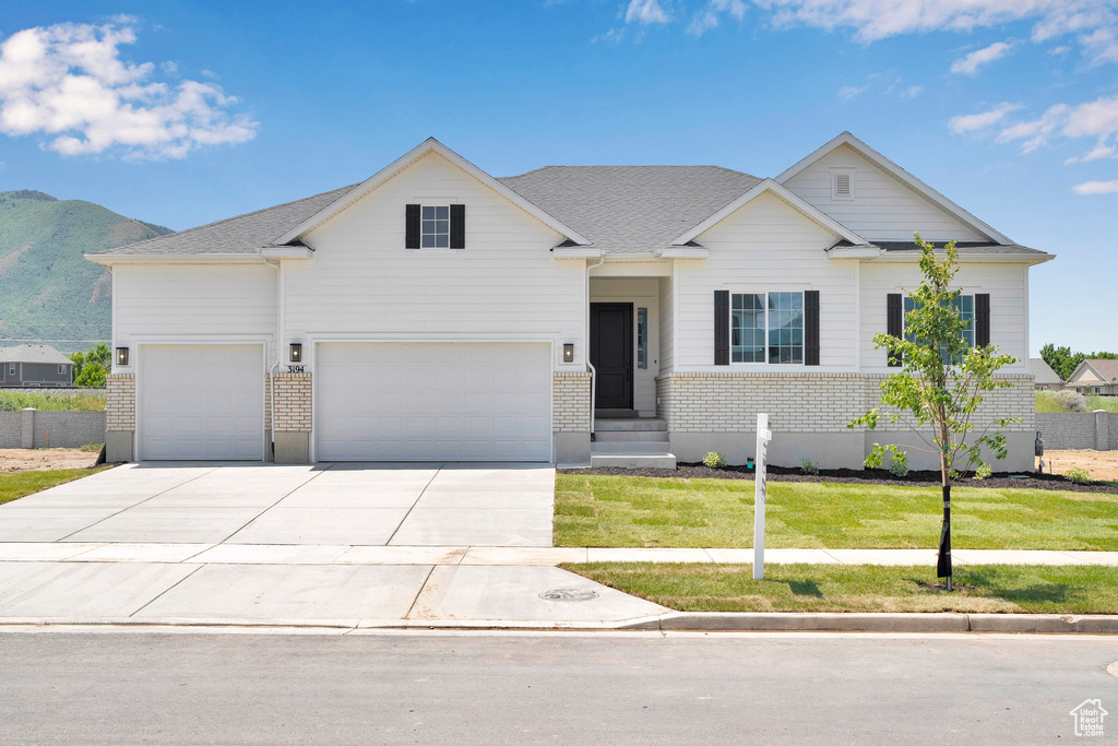 View of front facade with driveway, a front yard, an attached garage, a mountain view, and brick siding