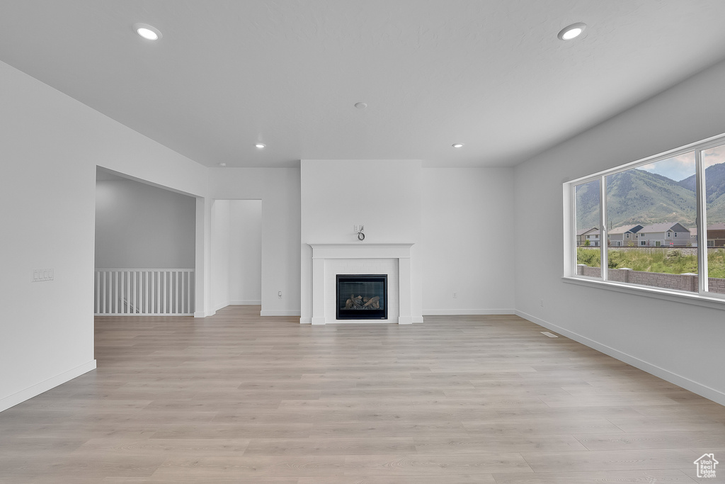 Unfurnished living room featuring recessed lighting, baseboards, light wood-type flooring, and a glass covered fireplace