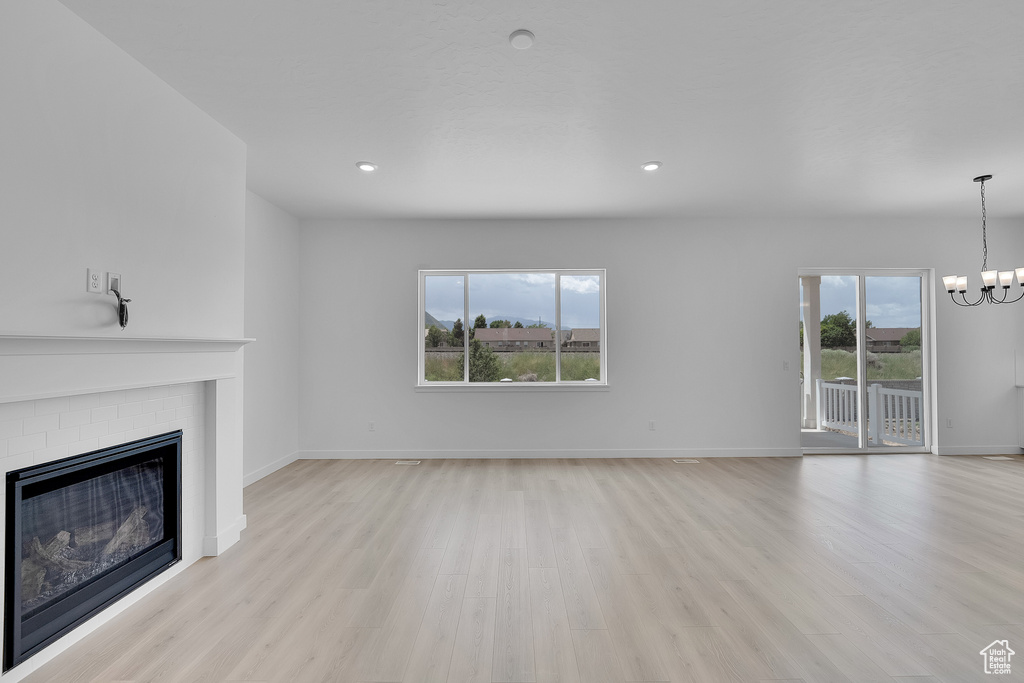 Unfurnished living room featuring a chandelier, light wood-type flooring, a fireplace, baseboards, and recessed lighting