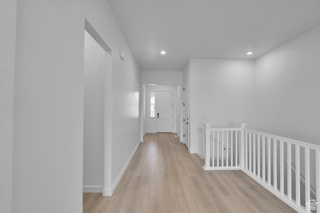 Hall with light wood finished floors, recessed lighting, baseboards, and an upstairs landing