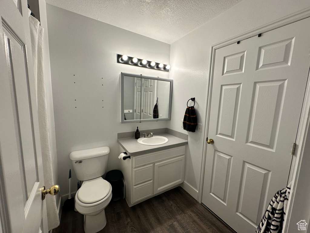 Full bathroom featuring a textured ceiling, vanity, toilet, and wood finished floors