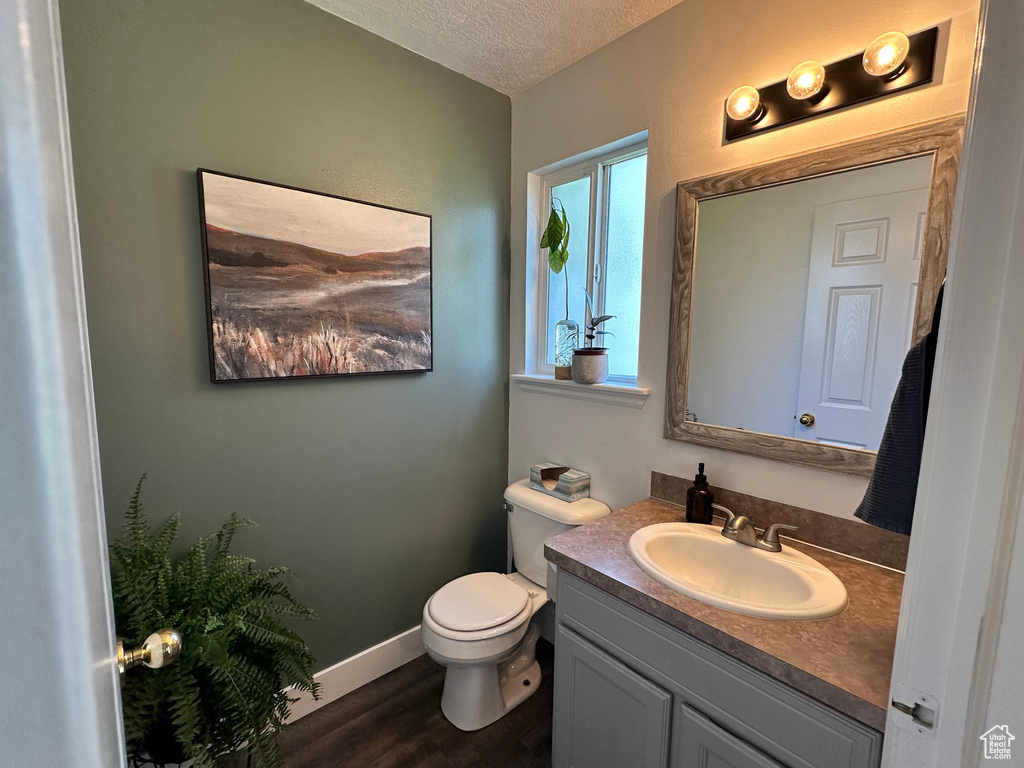 Half bathroom featuring vanity, toilet, a textured ceiling, wood finished floors, and baseboards