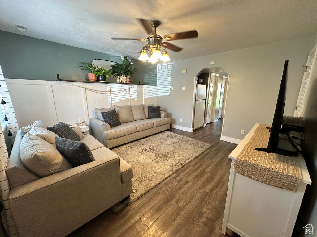 Living room featuring a ceiling fan, arched walkways, dark wood-style floors, a textured ceiling, and baseboards