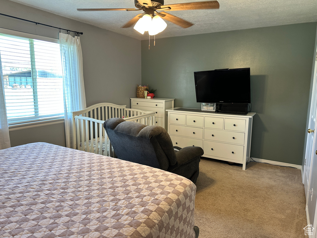 Bedroom with a textured ceiling, multiple windows, light colored carpet, and a ceiling fan
