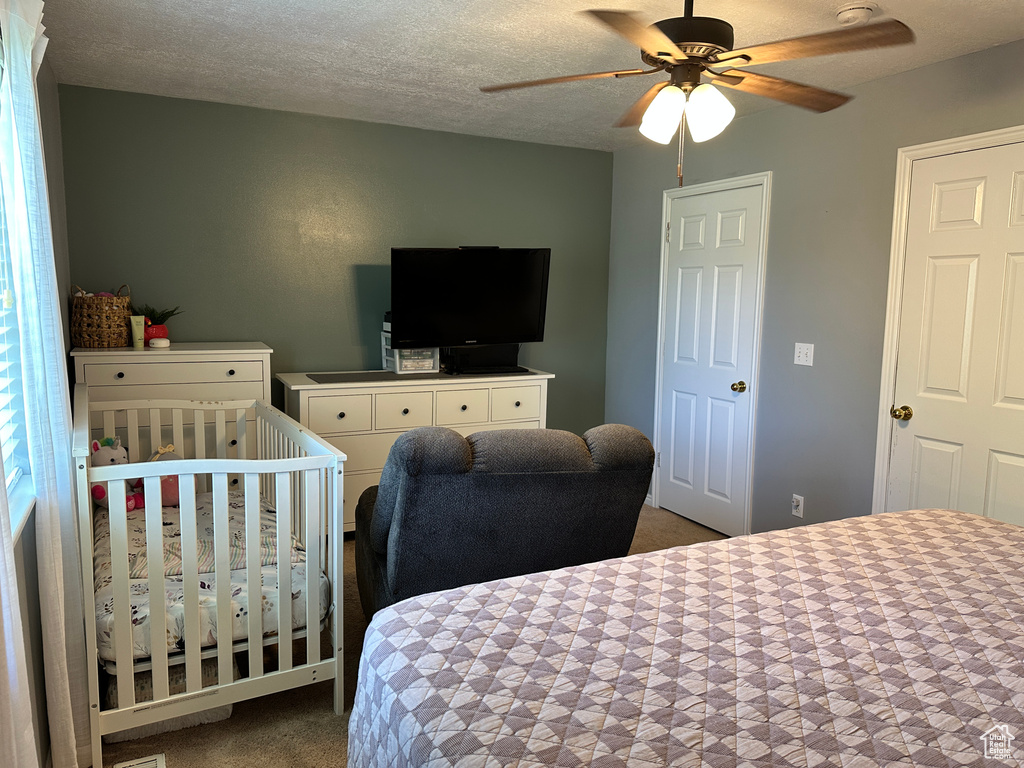 Carpeted bedroom with a ceiling fan and a crib