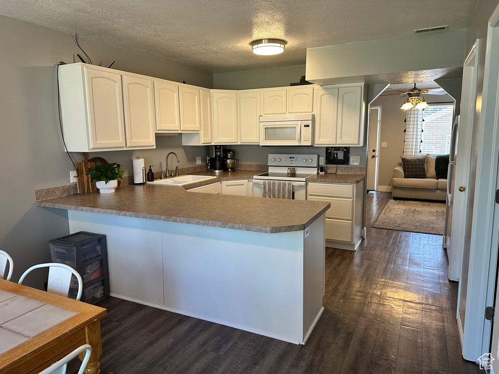 Kitchen with white appliances, a sink, a ceiling fan, a peninsula, and dark wood-type flooring