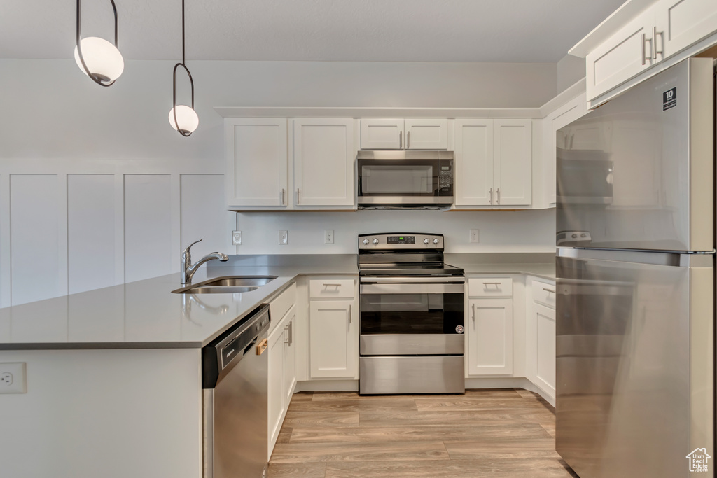 Kitchen featuring stainless steel appliances, a sink, a peninsula, light wood-style flooring, and white cabinets