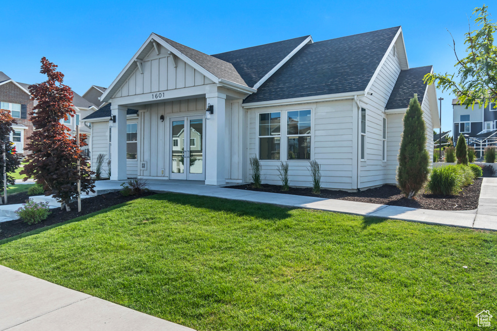 View of front facade with french doors, board and batten siding, a front lawn, and a shingled roof