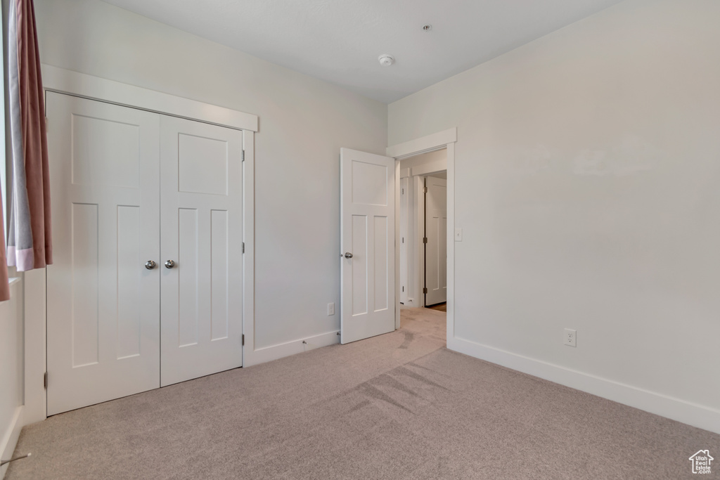 Unfurnished bedroom with light carpet, baseboards, and a closet
