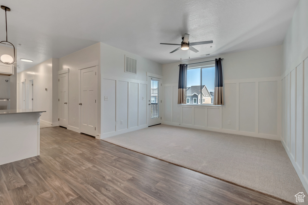 Unfurnished living room with a decorative wall, a ceiling fan, light wood-style flooring, and a wainscoted wall