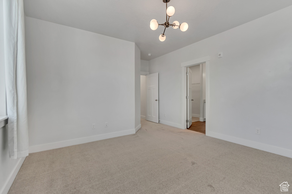 Carpeted spare room with a chandelier and baseboards