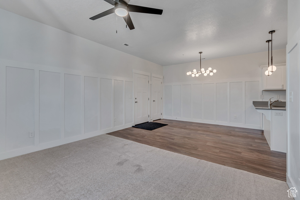 Carpeted spare room with a decorative wall, a ceiling fan, a chandelier, a sink, and wainscoting