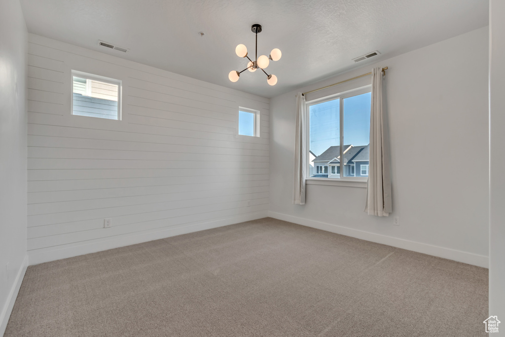Carpeted spare room featuring a chandelier, wood walls, and baseboards