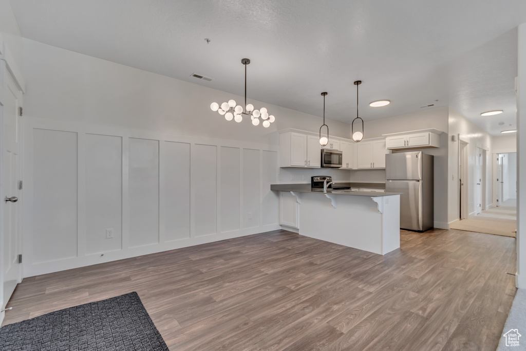 Kitchen featuring appliances with stainless steel finishes, a decorative wall, a peninsula, a kitchen breakfast bar, and light wood-type flooring