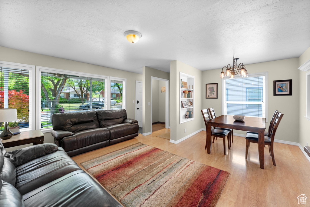 Living area featuring a chandelier, light wood-style flooring, baseboards, and a textured ceiling