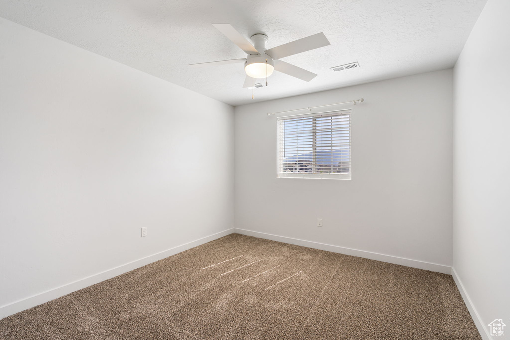 Carpeted empty room featuring baseboards, a ceiling fan, and a textured ceiling