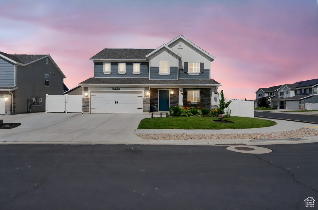 View of front facade with driveway, an attached garage, stone siding, a gate, and board and batten siding