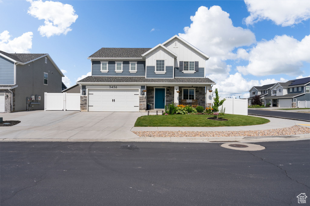 View of front of property with driveway, stone siding, an attached garage, and board and batten siding