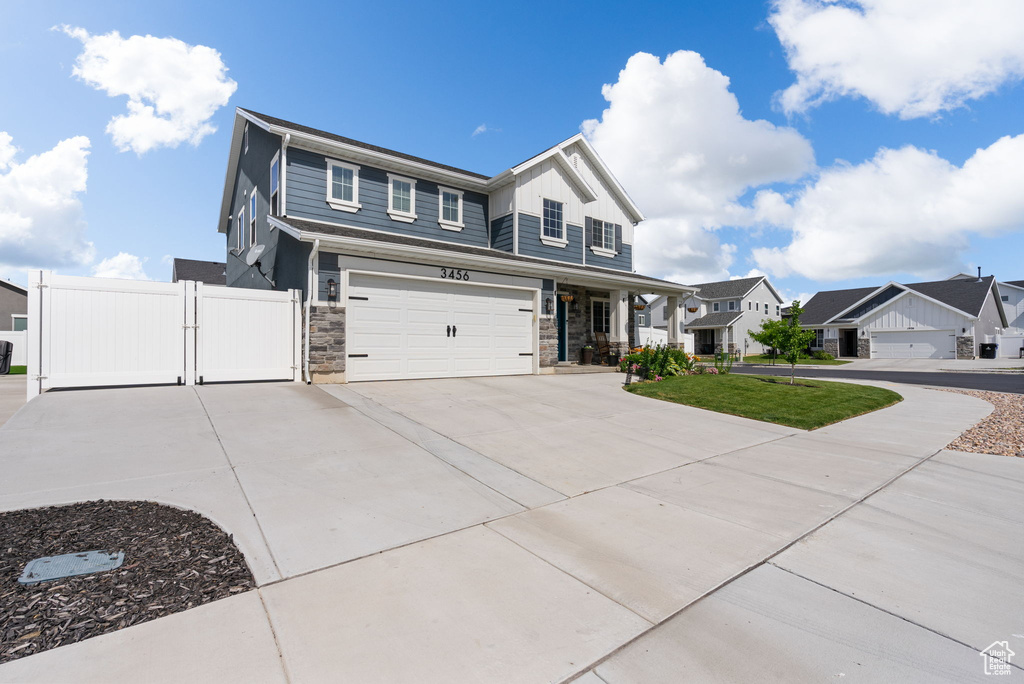 View of front of house featuring an attached garage, stone siding, a gate, driveway, and a porch