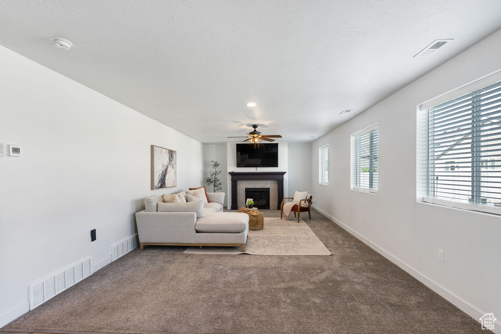 Carpeted living area with a fireplace with raised hearth, a ceiling fan, and baseboards