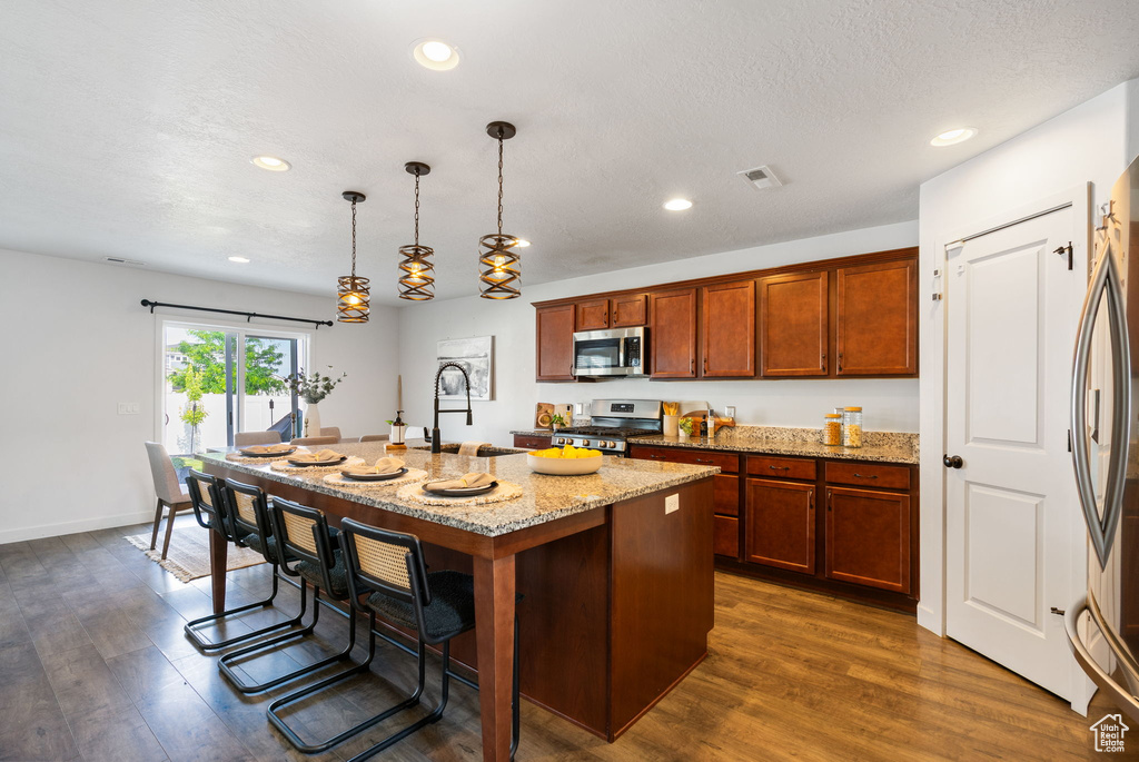 Kitchen featuring appliances with stainless steel finishes, a sink, a kitchen island with sink, a kitchen breakfast bar, and light stone counters