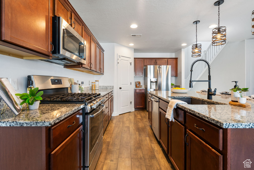 Kitchen with appliances with stainless steel finishes, a sink, hardwood / wood-style flooring, recessed lighting, and decorative light fixtures
