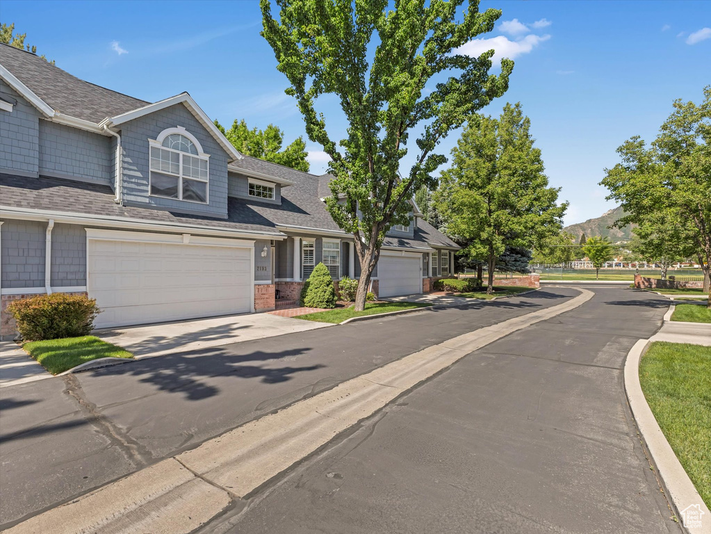 View of front facade with driveway, brick siding, a mountain view, an attached garage, and roof with shingles