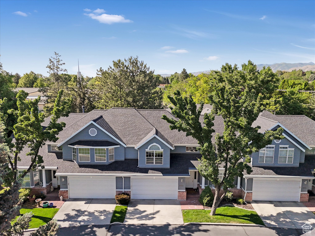 View of front facade featuring a garage, driveway, brick siding, and a shingled roof