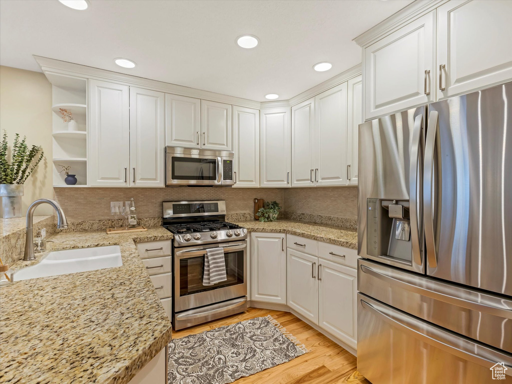 Kitchen featuring appliances with stainless steel finishes, a sink, white cabinets, open shelves, and decorative backsplash