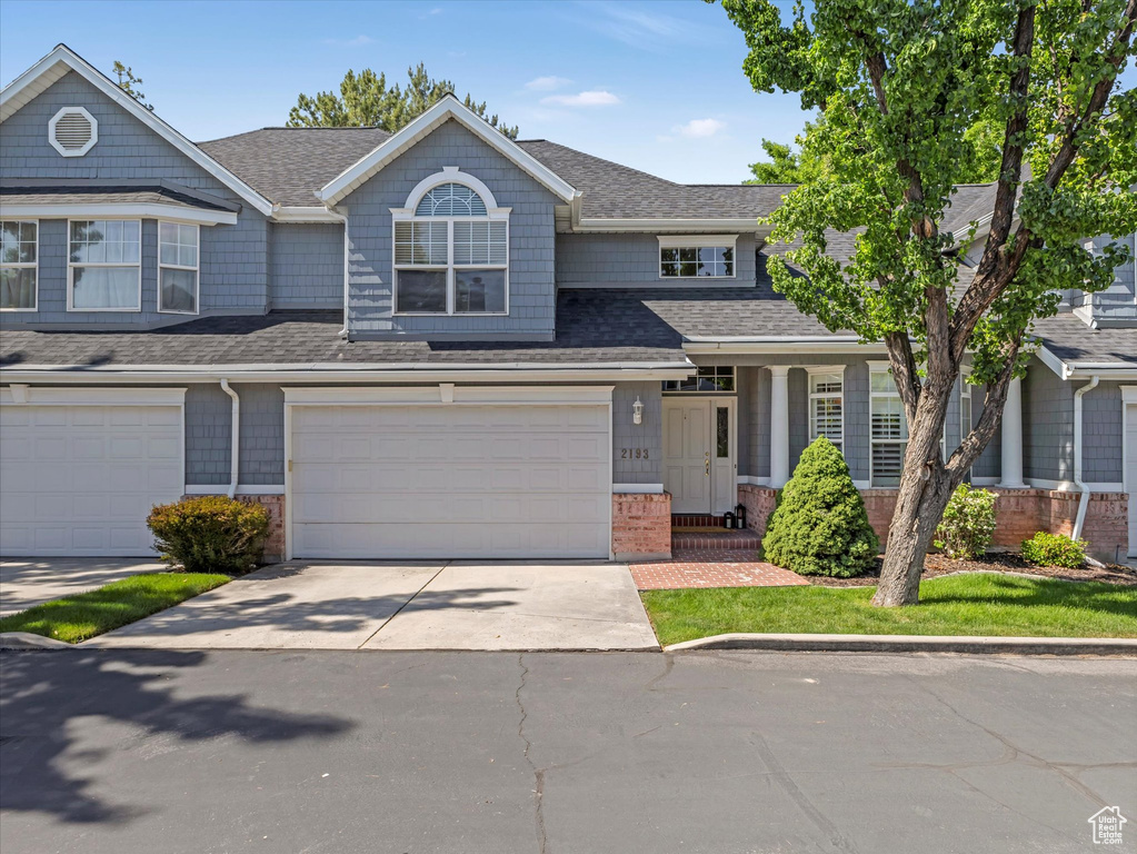 View of front of home with driveway, a garage, a shingled roof, and brick siding