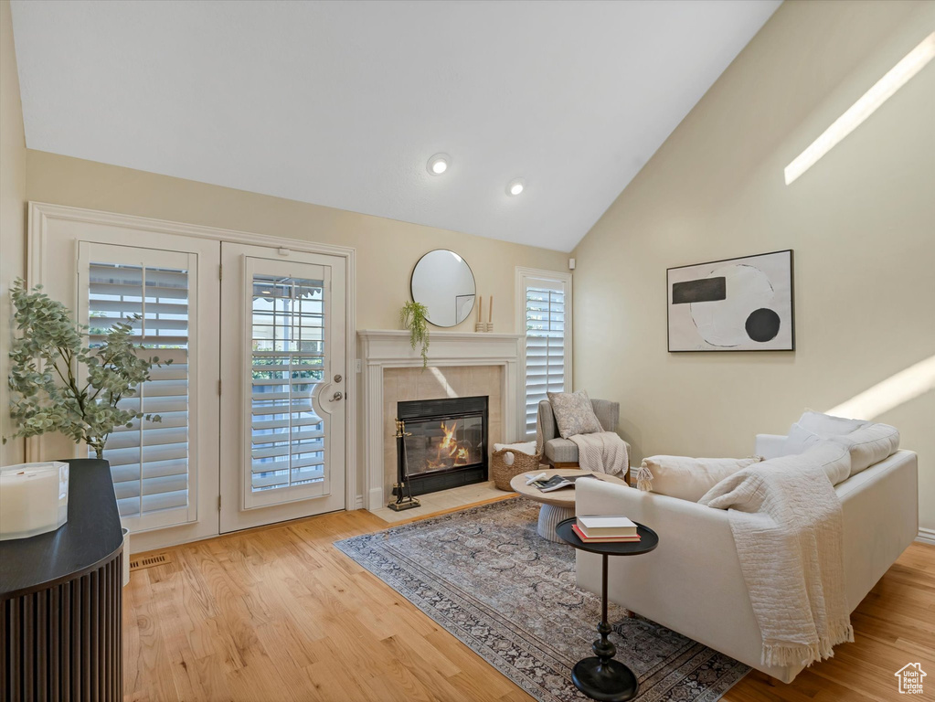 Living room with wood finished floors, a tile fireplace, high vaulted ceiling, and recessed lighting