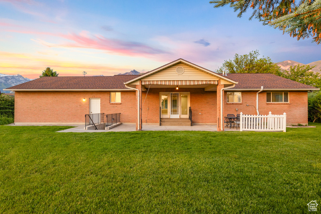 Rear view of house with a patio, a yard, brick siding, and a mountain view