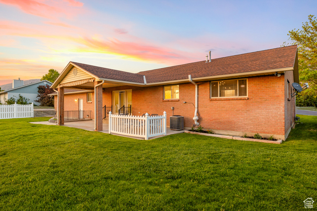 Back of property at dusk with a patio area, brick siding, roof with shingles, and central AC
