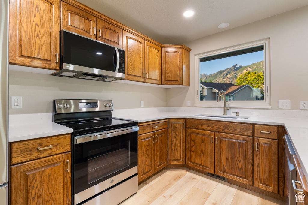 Kitchen featuring appliances with stainless steel finishes, a sink, brown cabinetry, light wood-style flooring, and recessed lighting