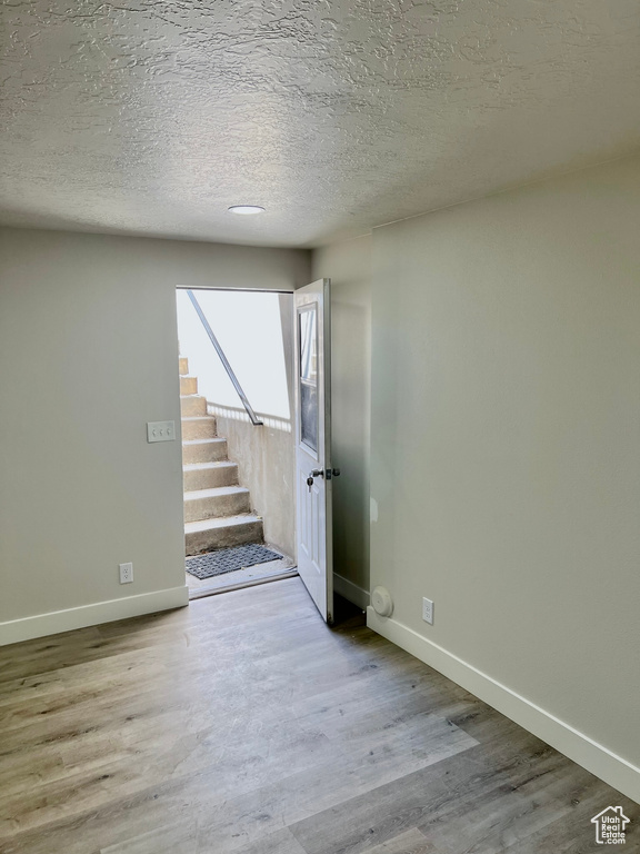 Empty room with baseboards, wood finished floors, stairs, and a textured ceiling