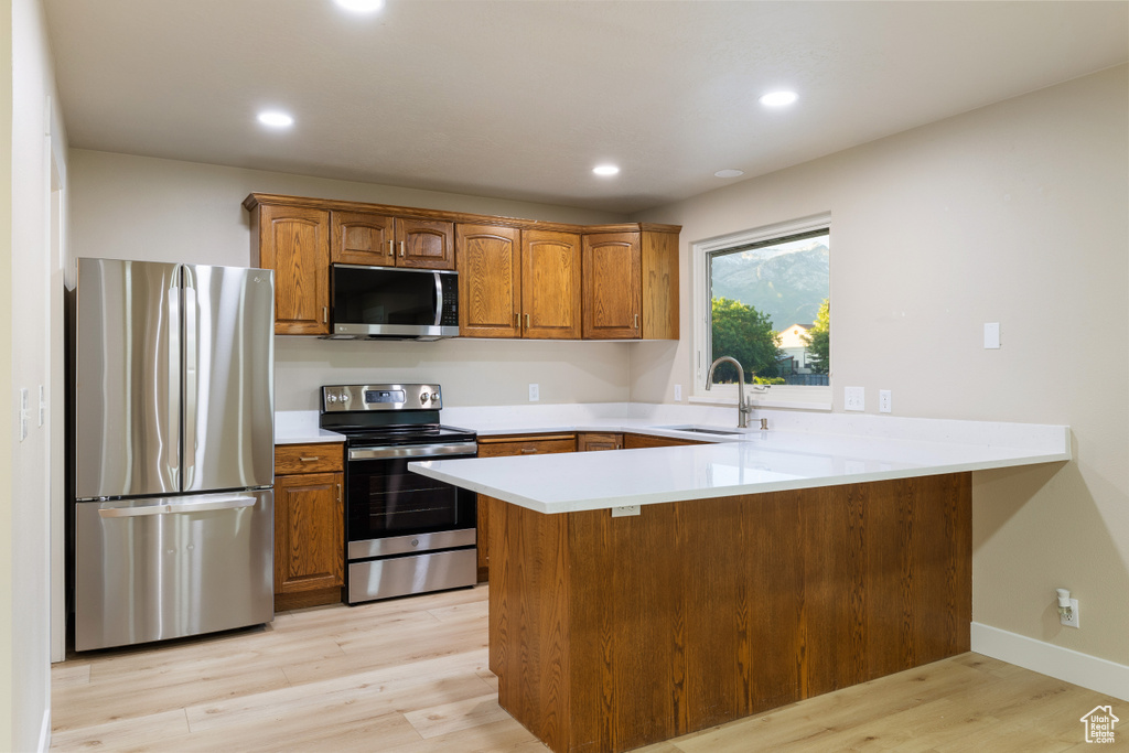 Kitchen featuring appliances with stainless steel finishes, a peninsula, brown cabinetry, light wood finished floors, and recessed lighting
