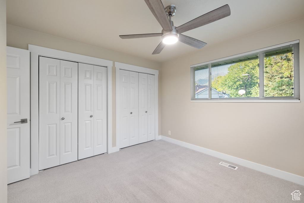 Unfurnished bedroom with multiple closets, light carpet, baseboards, and a ceiling fan