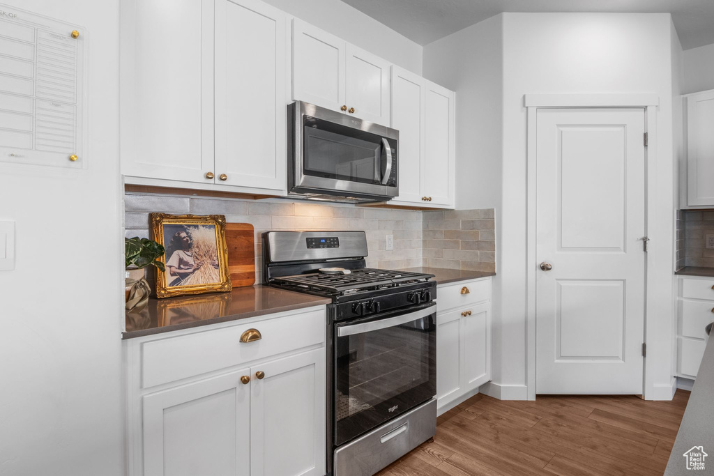 Kitchen featuring stainless steel appliances, dark countertops, wood finished floors, and decorative backsplash