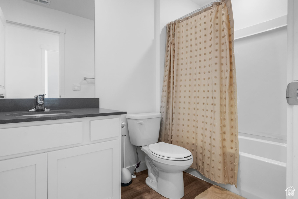 Bathroom featuring vanity, wood finished floors, shower / bath combo, and toilet